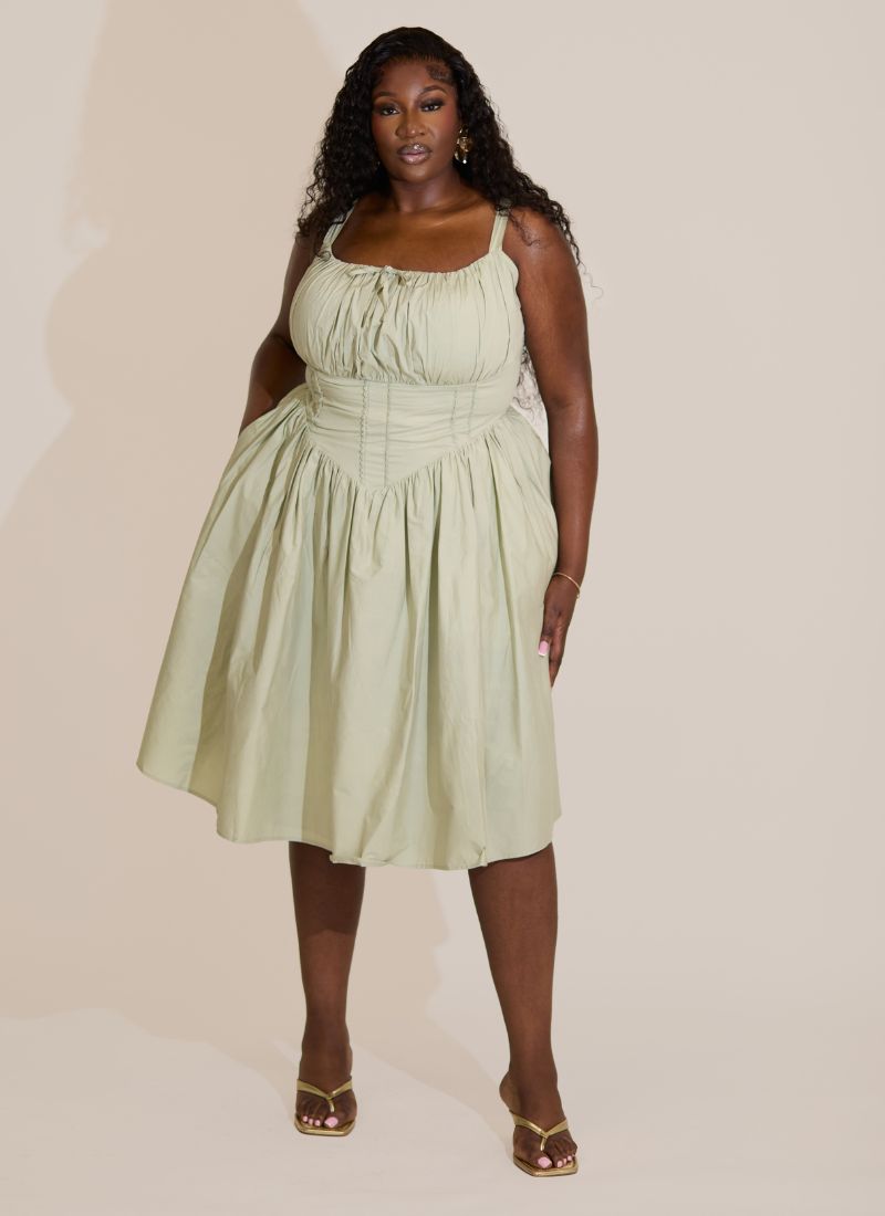 Woman wearing a light green sage fuller bust midi cotton dress against a plain background